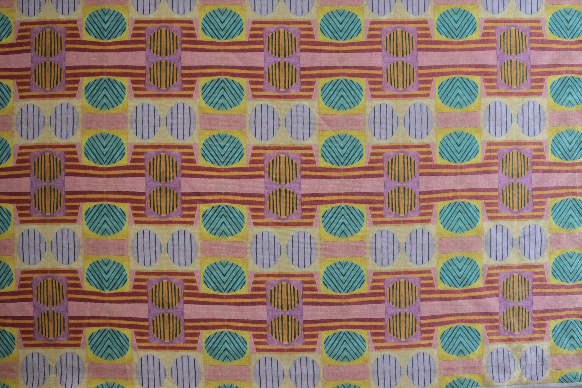 Close up of printed fabric with a complex geometric and striped pattern with pink, orange, turquoise and red. 