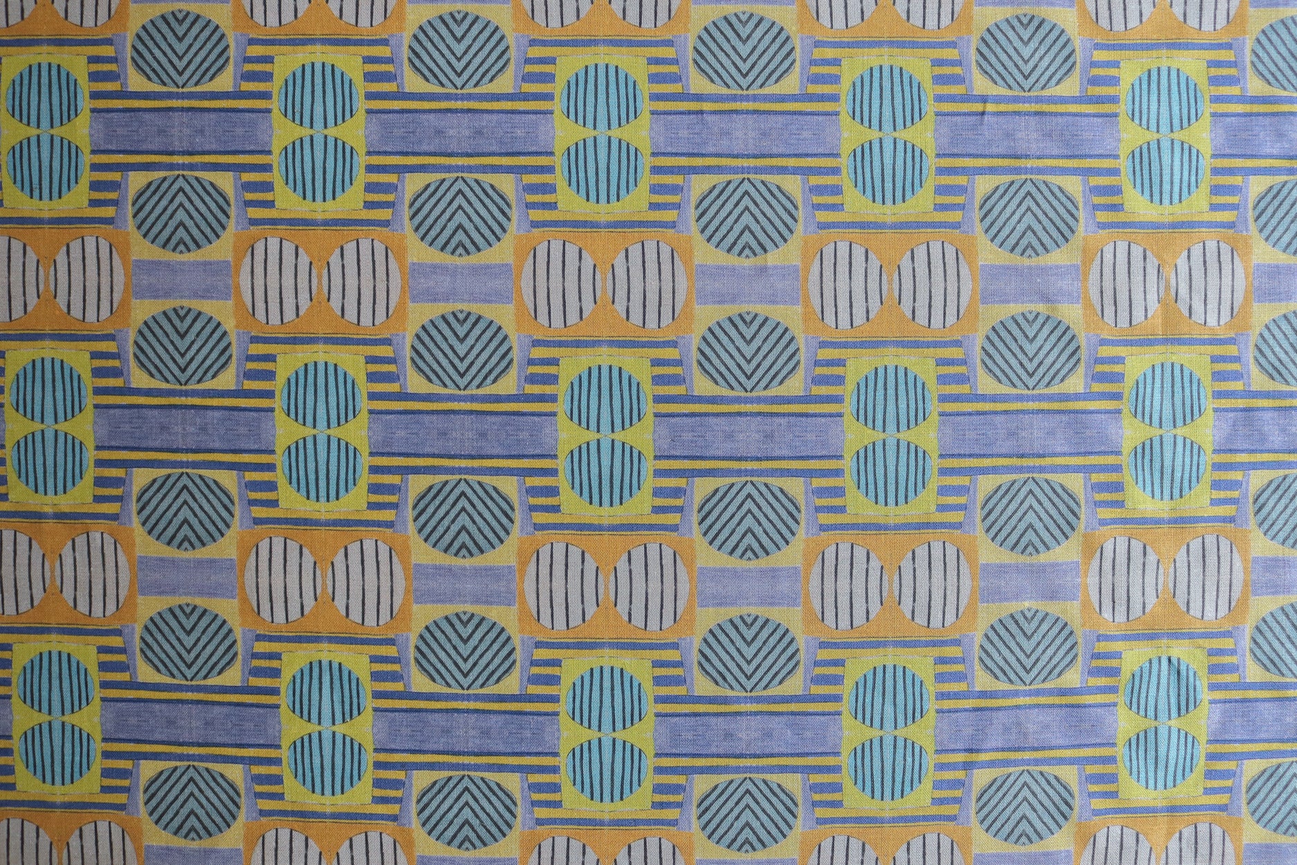 Close up of printed fabric with a complex geometric and striped pattern with yellow, blue, orange and pale blue 