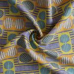 Close up of gently draped printed fabric with a complex geometric and striped pattern with yellow, blue, orange and pale pink. 