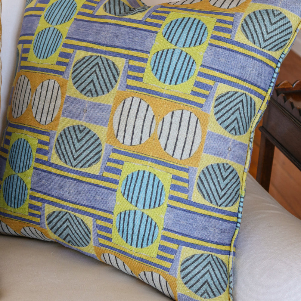 Close up of white couch with a bold geometric patterned pillow in yellow, orange and blue.