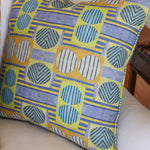 Close up of white couch with a bold geometric patterned pillow in yellow, orange and blue.