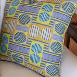 Close up of white couch with a bold geometric patterned pillow in yellow, orange and blue.