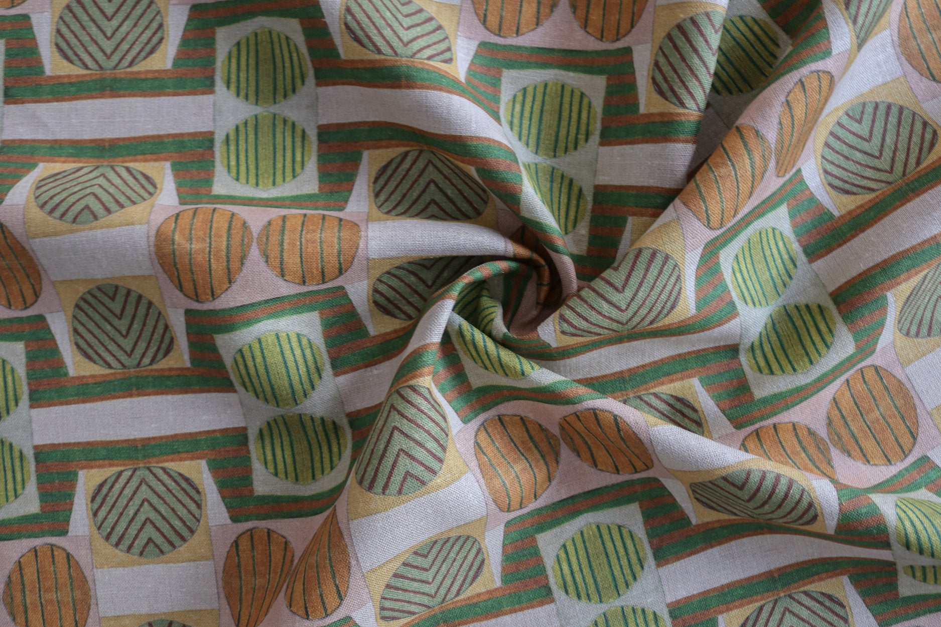 Close up of gently draped printed fabric with a complex geometric and striped pattern with orange, brown, grey and green.