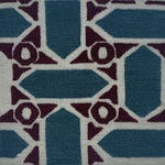 A close-up of a handwoven rug featuring geometric shapes in slate blue, deep plum, and off-white.