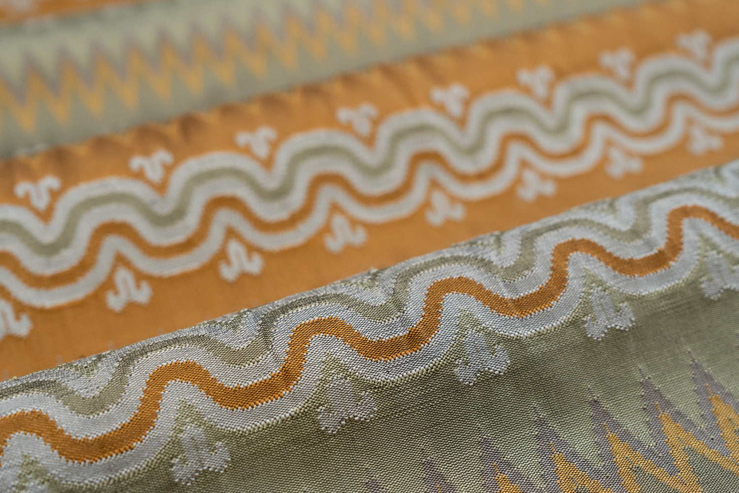 Close-up of patterned fabric with wavy lines and geometric shapes in orange, ivory and green. 