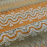 Close-up of patterned fabric with wavy lines and geometric shapes in orange, ivory and green. 