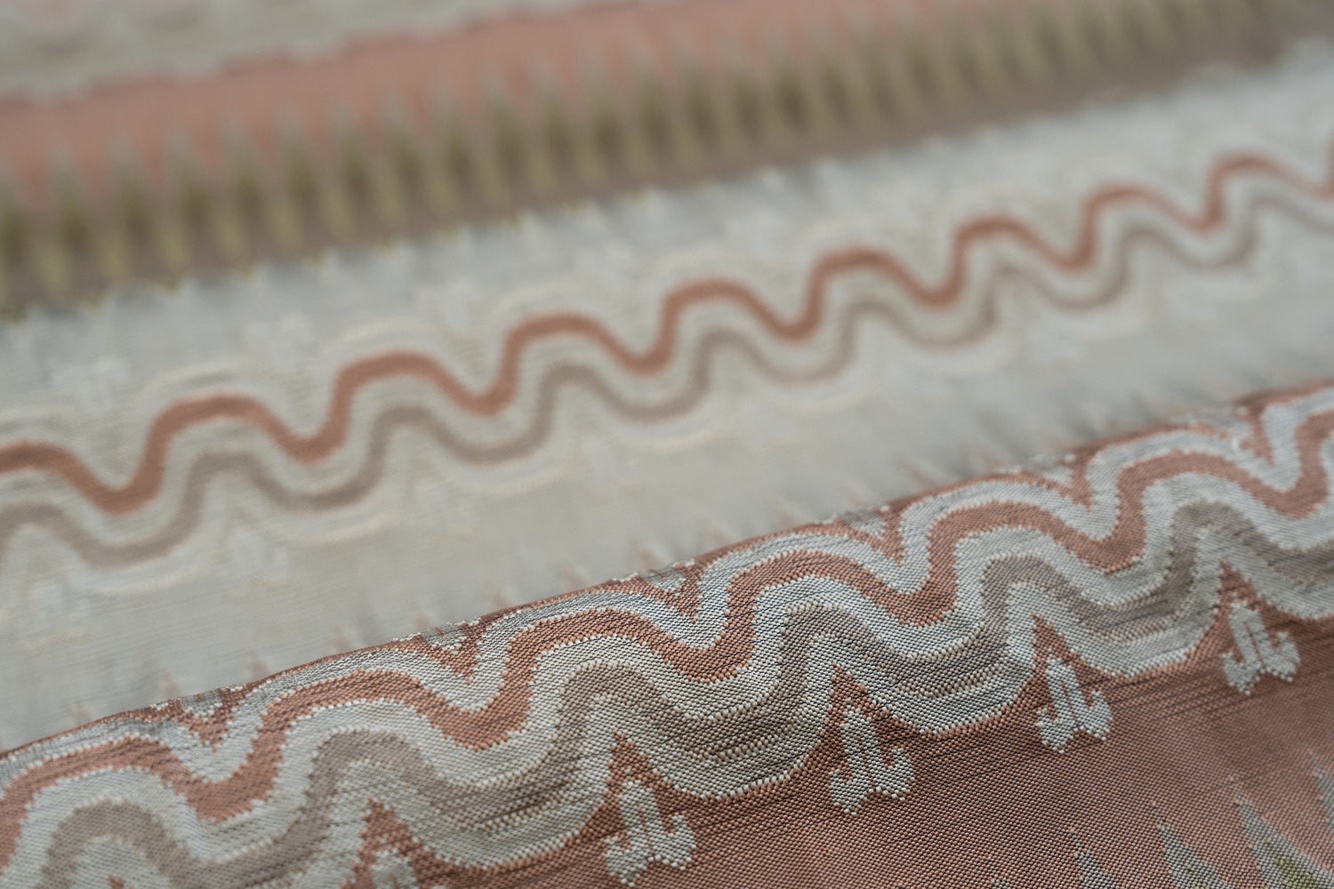 Close-up of patterned fabric with wavy lines and geometric shapes in pink, cream and beige. 