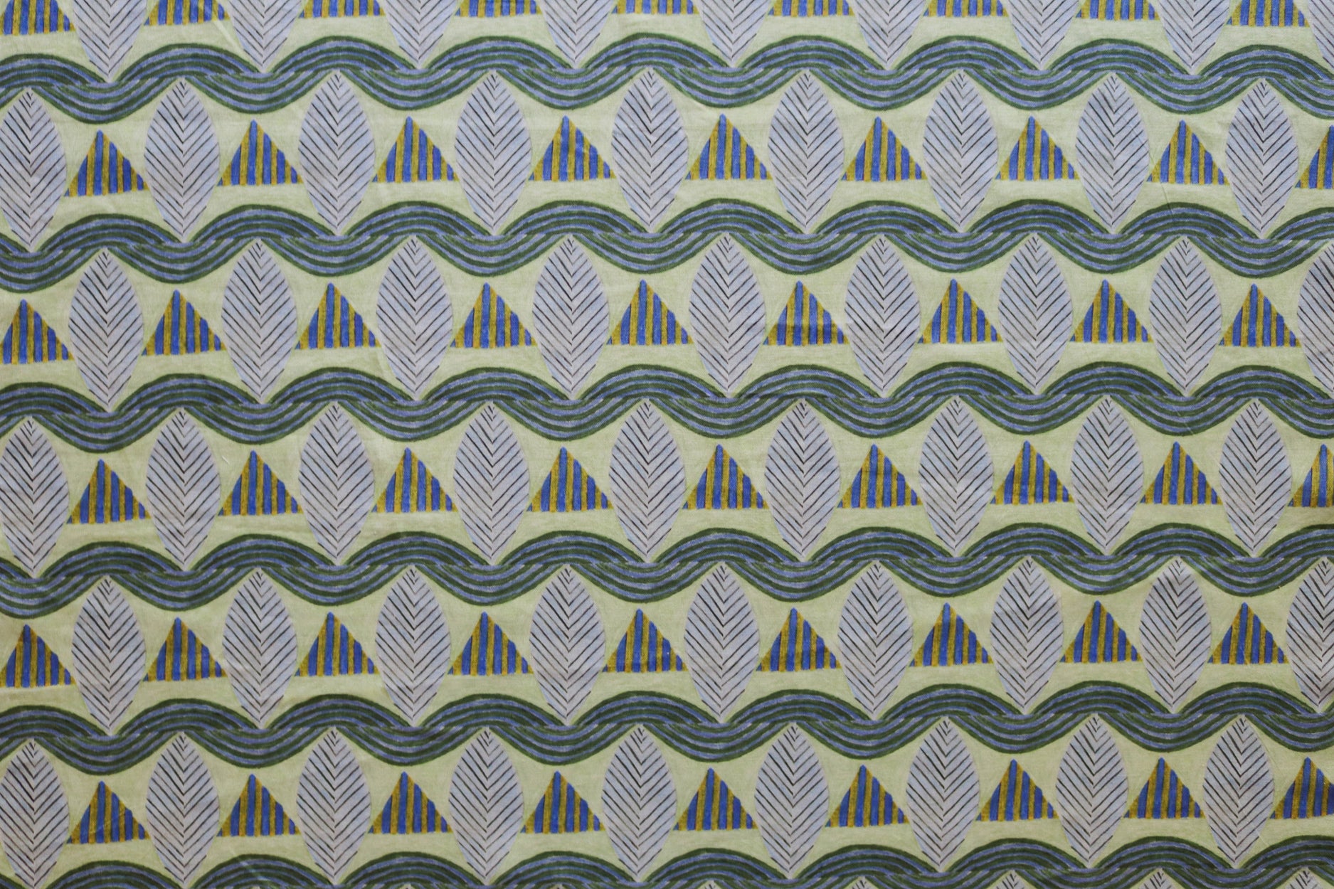 A close-up of a patterned fabric featuring repeating rows of stylized grey leaves, blue and yellow stripe triangles and wavy blue-yellow lines on yellow background.