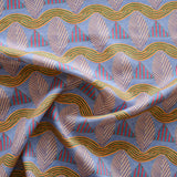 A close-up of a gently draped patterned fabric featuring repeating rows of stylized pink leaves, blue and red striped triangles and wavy orange-green lines on a blue background