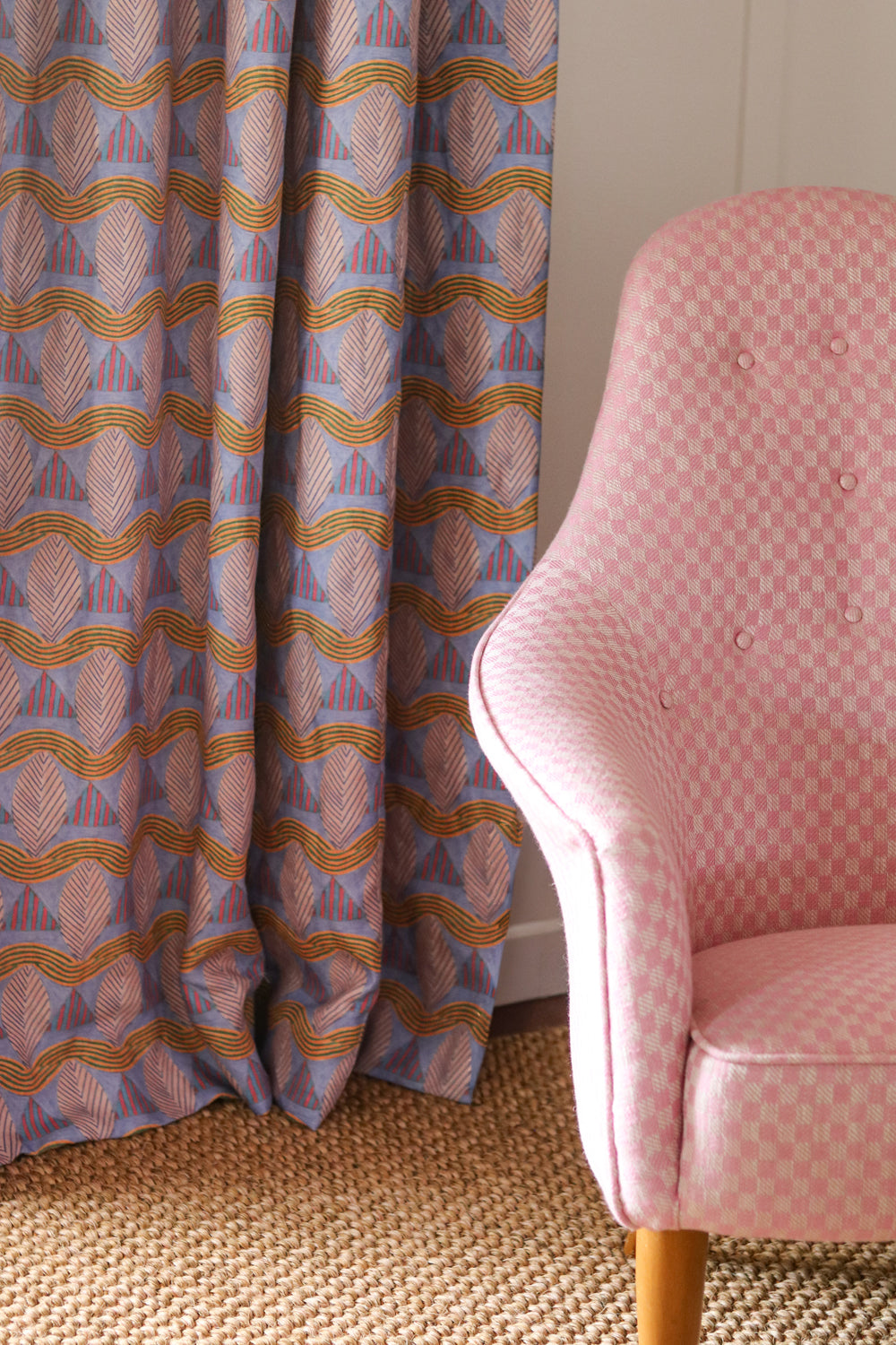 Detail of a living room with a pink checker pattern side chair, sisal rug and geometric striped leaf pattern in pink, blue and purple.