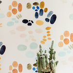 A cactus stands in front of a wall papered in an abstract painterly print in turquoise, blue, orange and white.