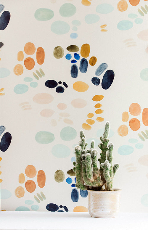 A cactus stands in front of a wall papered in an abstract painterly print in turquoise, blue, orange and white.
