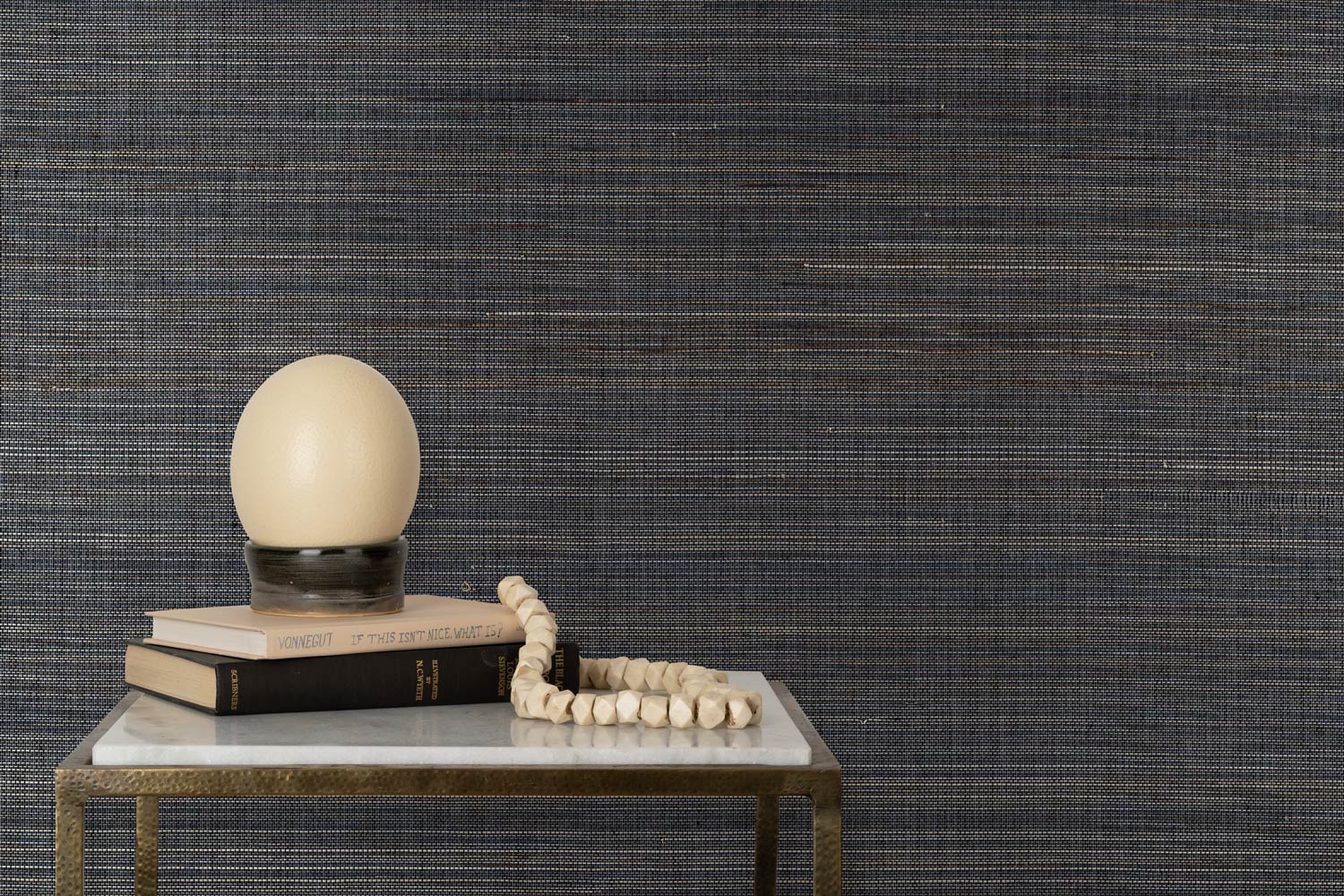 End table with books and a globe lamp in front of a wall papered in textured grasscloth in shades of grey, brown and black.