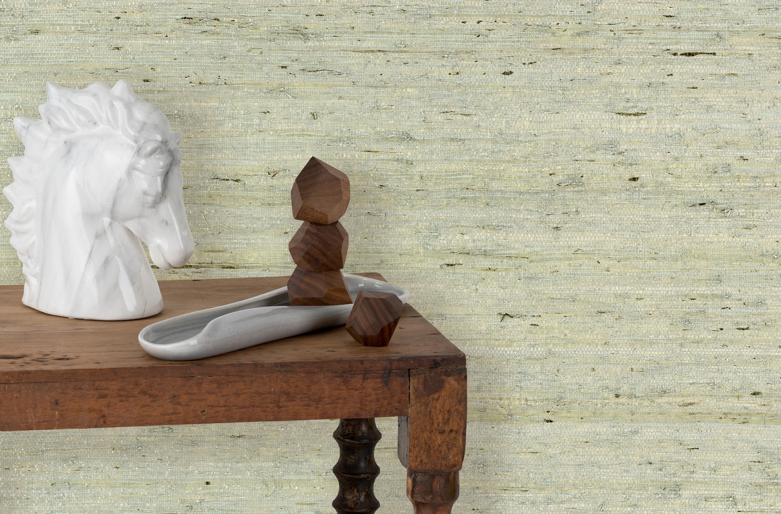 End table with marble and wood scupltures in front of a wall papered in textured pastel arrowroot grasscloth.