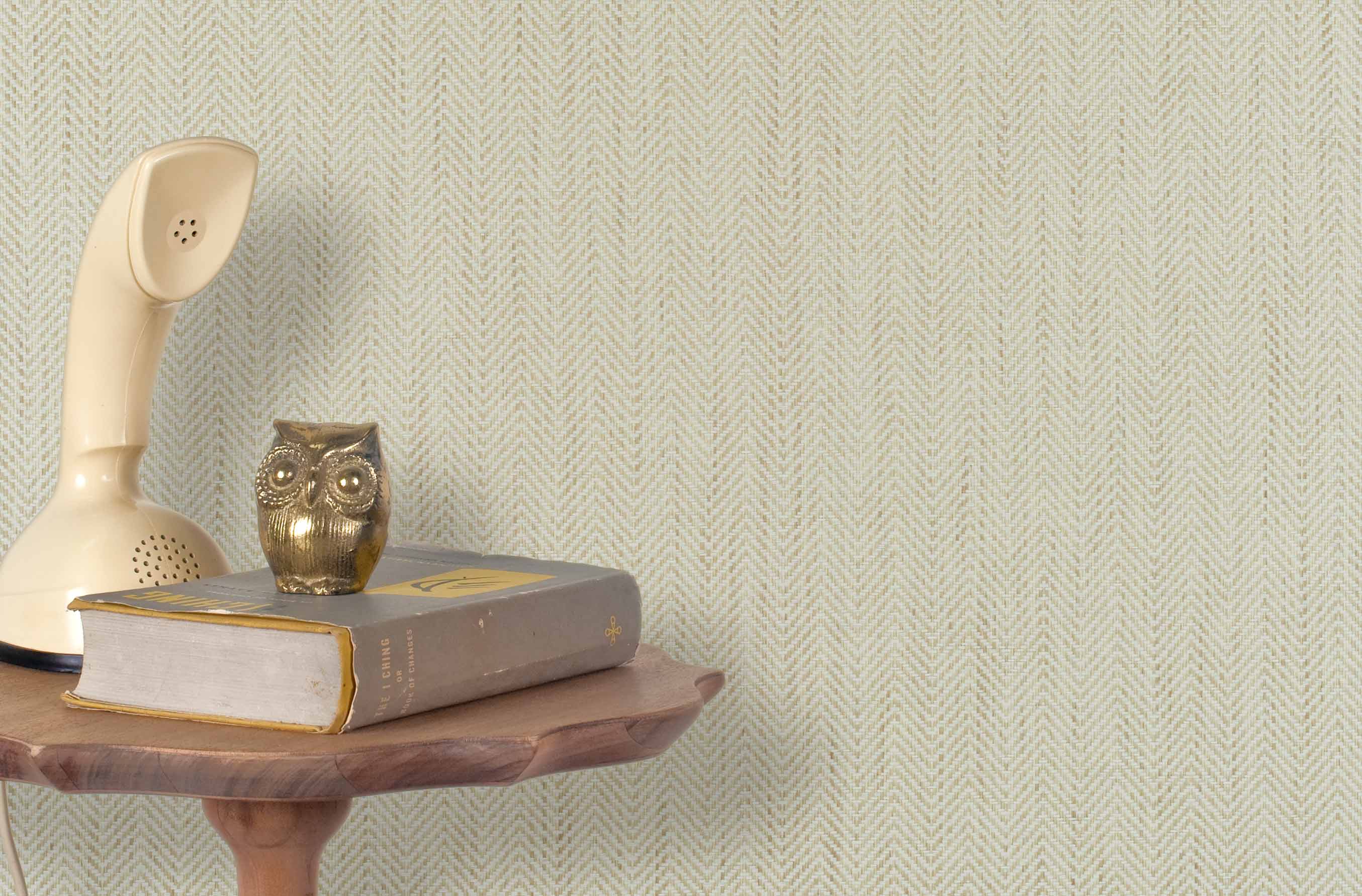 End table with books and  vintage phone in front of a grasscloth wallpaper with a herringbone weave in cream and beige.