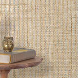 End table with a phone, book and owl sculpture in front of a wall covered in paperweave grasscloth in metallic tan and gray.
