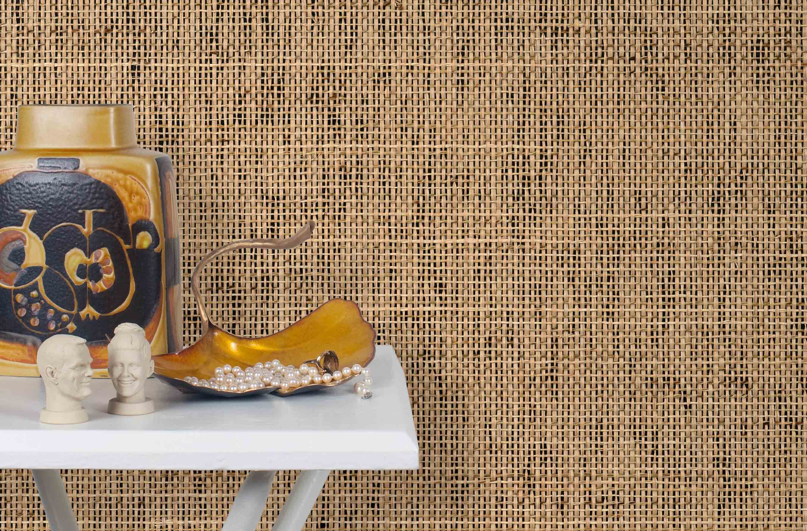 End table with a vase and sculptures in front of a wall papered in jute grasscloth.