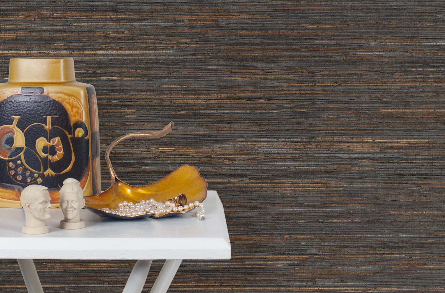 End table with a vase and sculptures in front of a wall papered in jute grasscloth in black and brown.