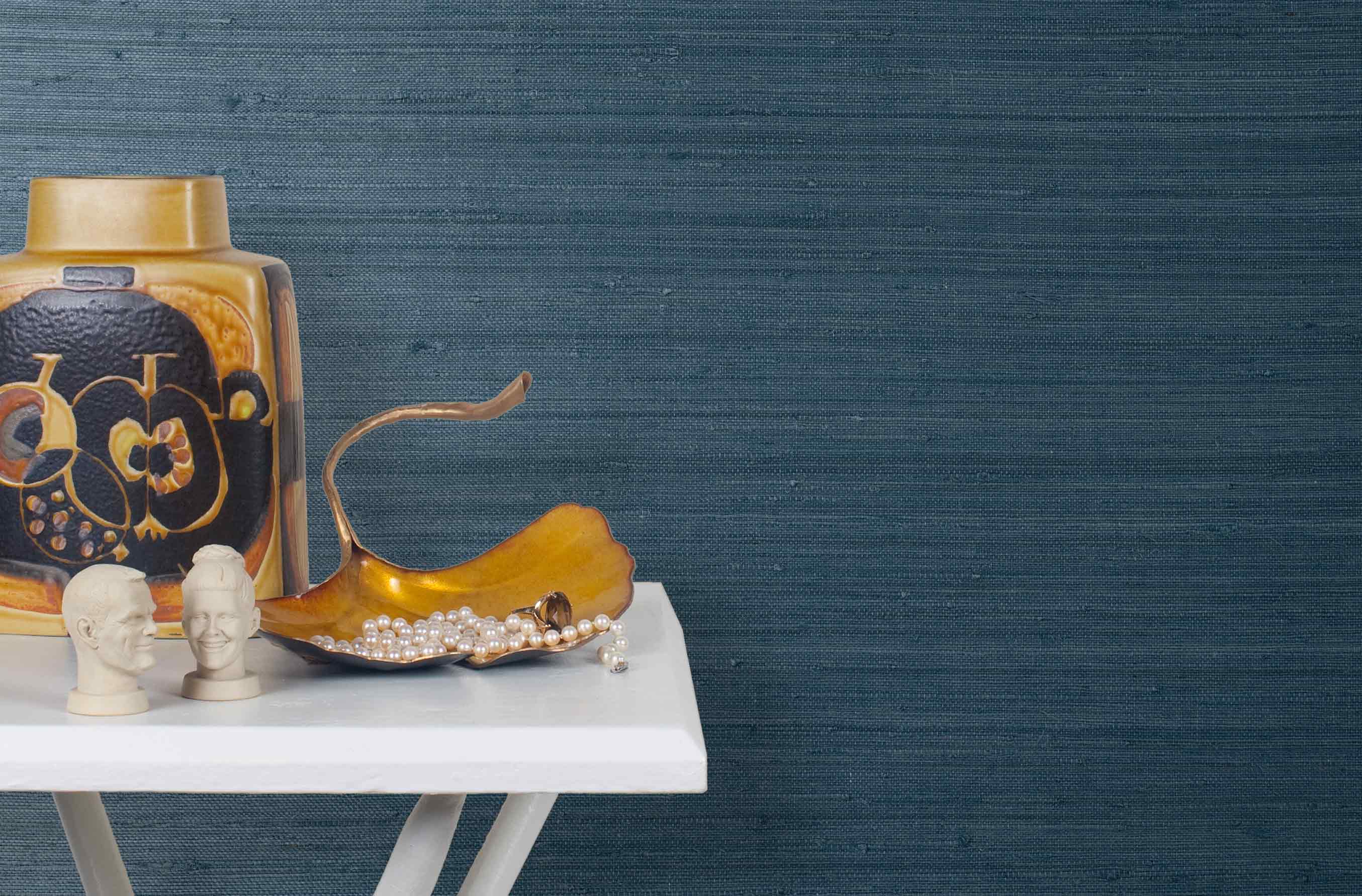 End table with a vase and sculptures in front of a wall papered in jute grasscloth in navy blue.