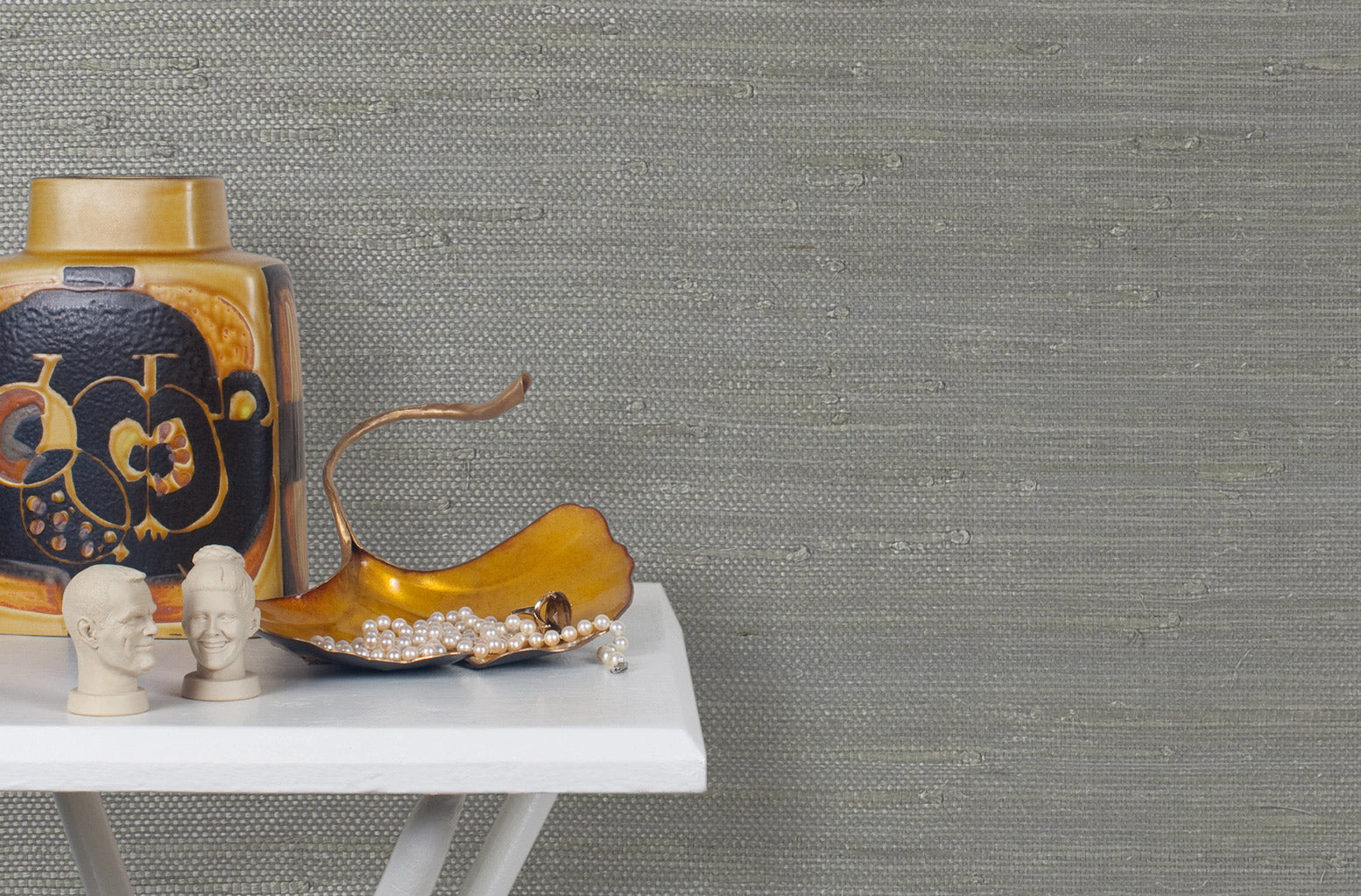 End table with a vase and sculptures in front of a wall papered in jute grasscloth in gray.