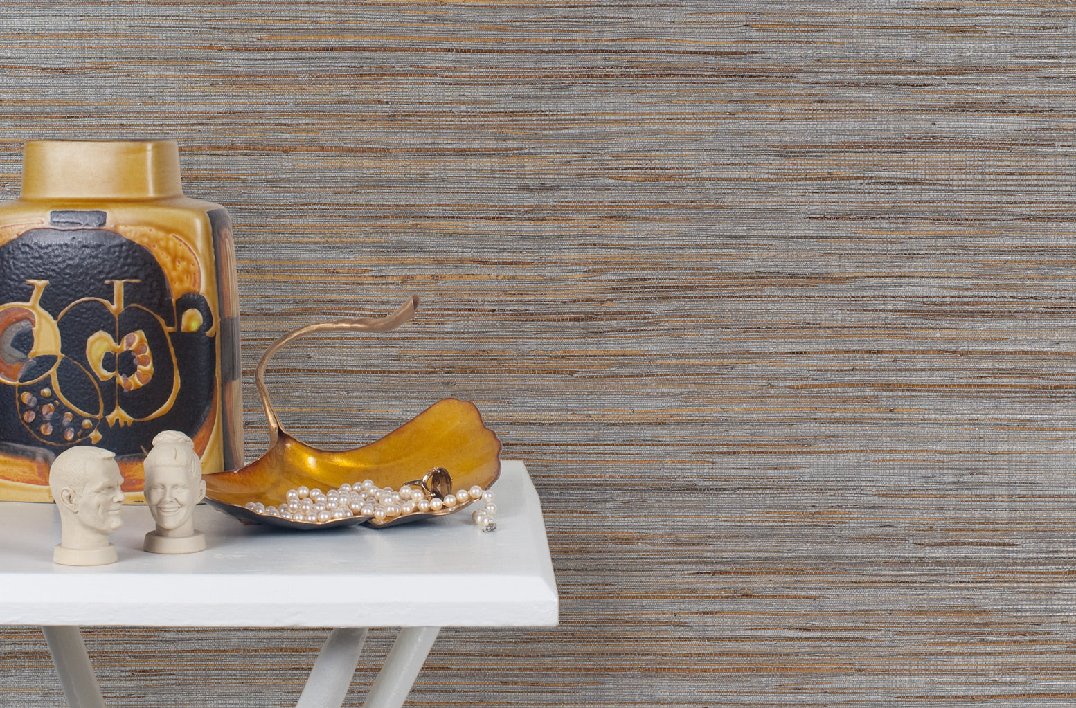 End table with a vase and sculptures in front of a wall papered in metallic-rubbed jute grasscloth in gray and tan.