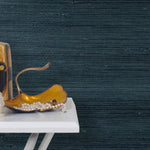 End table with a vase and sculptures in front of a wall papered in jute grasscloth in dark navy.