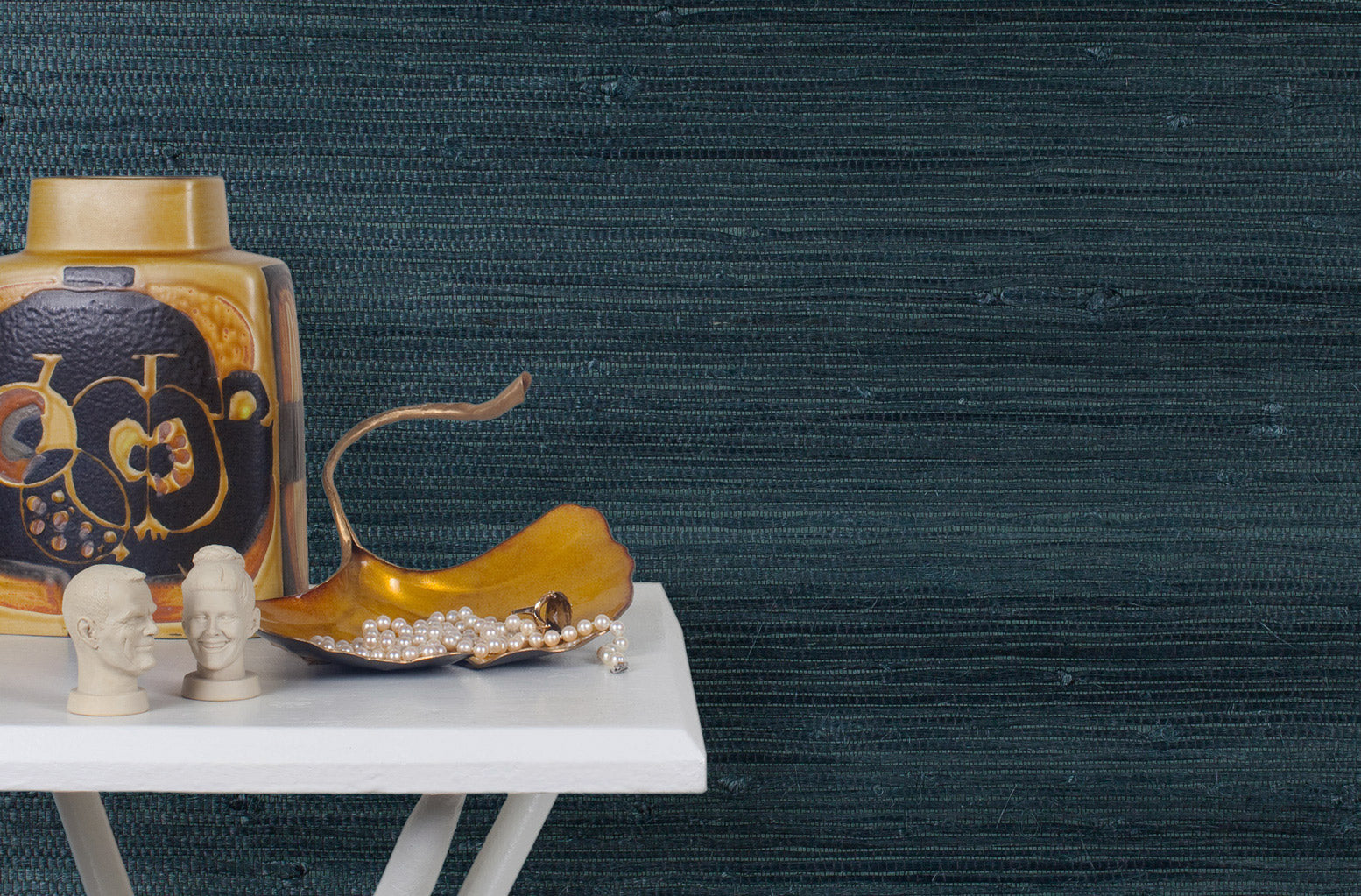 End table with a vase and sculptures in front of a wall papered in jute grasscloth in dark navy.