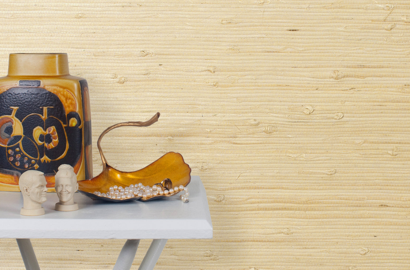 End table with a vase and sculptures in front of a wall papered in jute grasscloth in light tan.