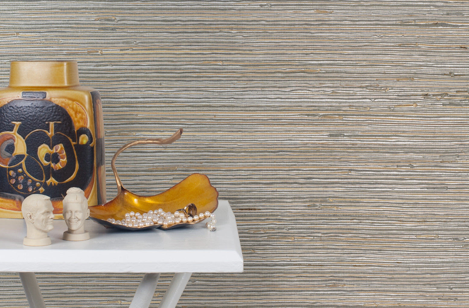 End table with a vase and sculptures in front of a wall papered in jute grasscloth in gray and tan.