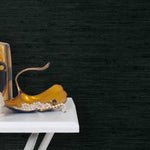 End table with a vase and sculptures in front of a wall papered in jute grasscloth in inky black.