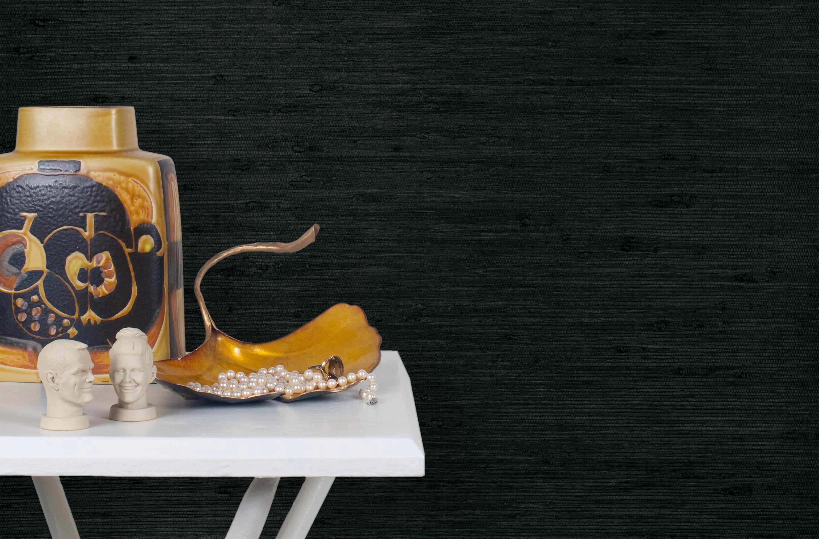 End table with a vase and sculptures in front of a wall papered in jute grasscloth in inky black.