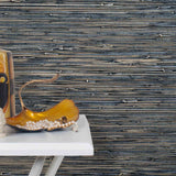 End table with a vase and sculptures in front of a wall papered in metallic-rubbed jute grasscloth in black and gray.