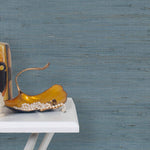 End table with a vase and sculptures in front of a wall papered in jute grasscloth in cadet blue.