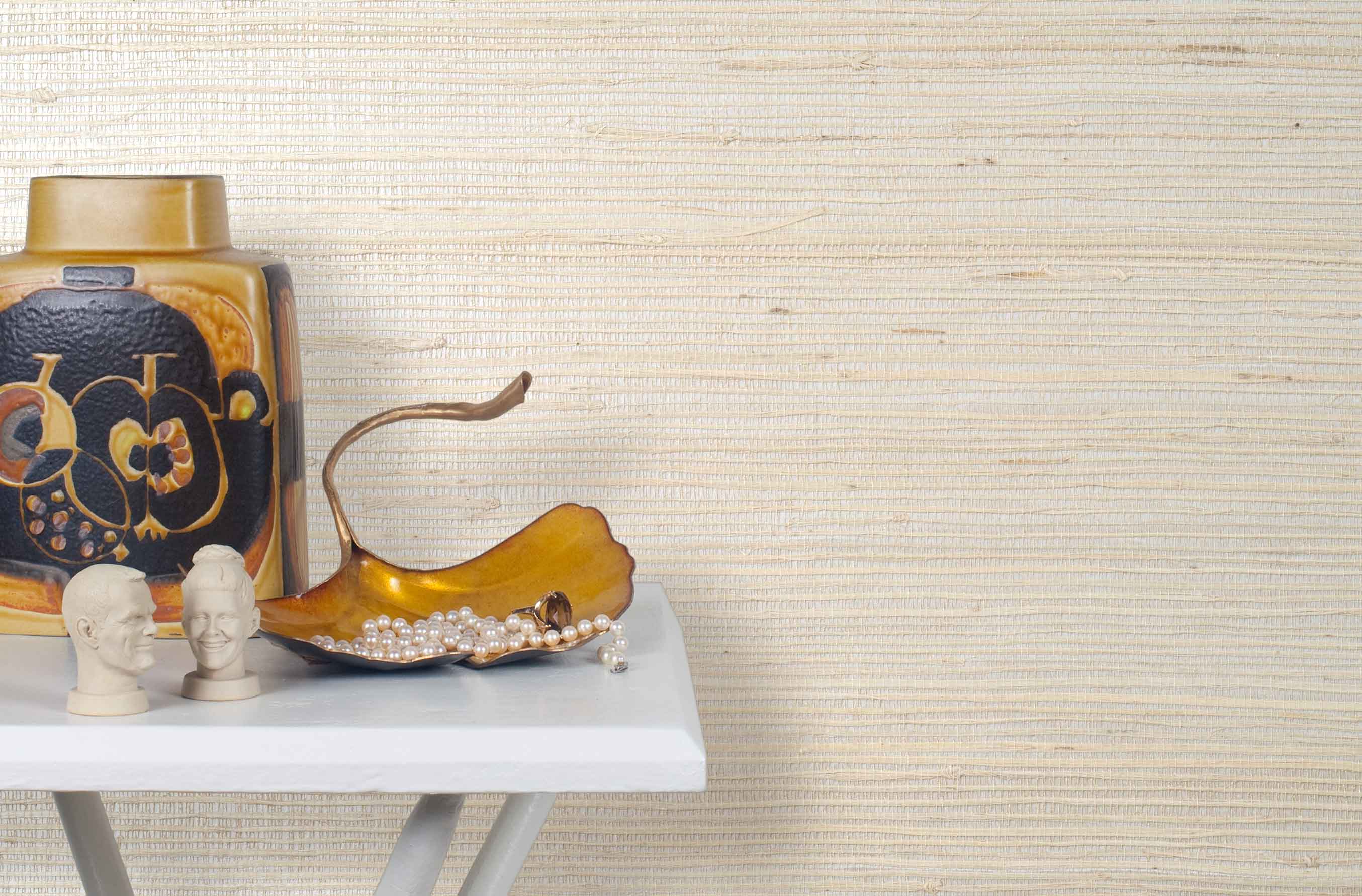 End table with a vase and sculptures in front of a wall papered in jute grasscloth in cream.