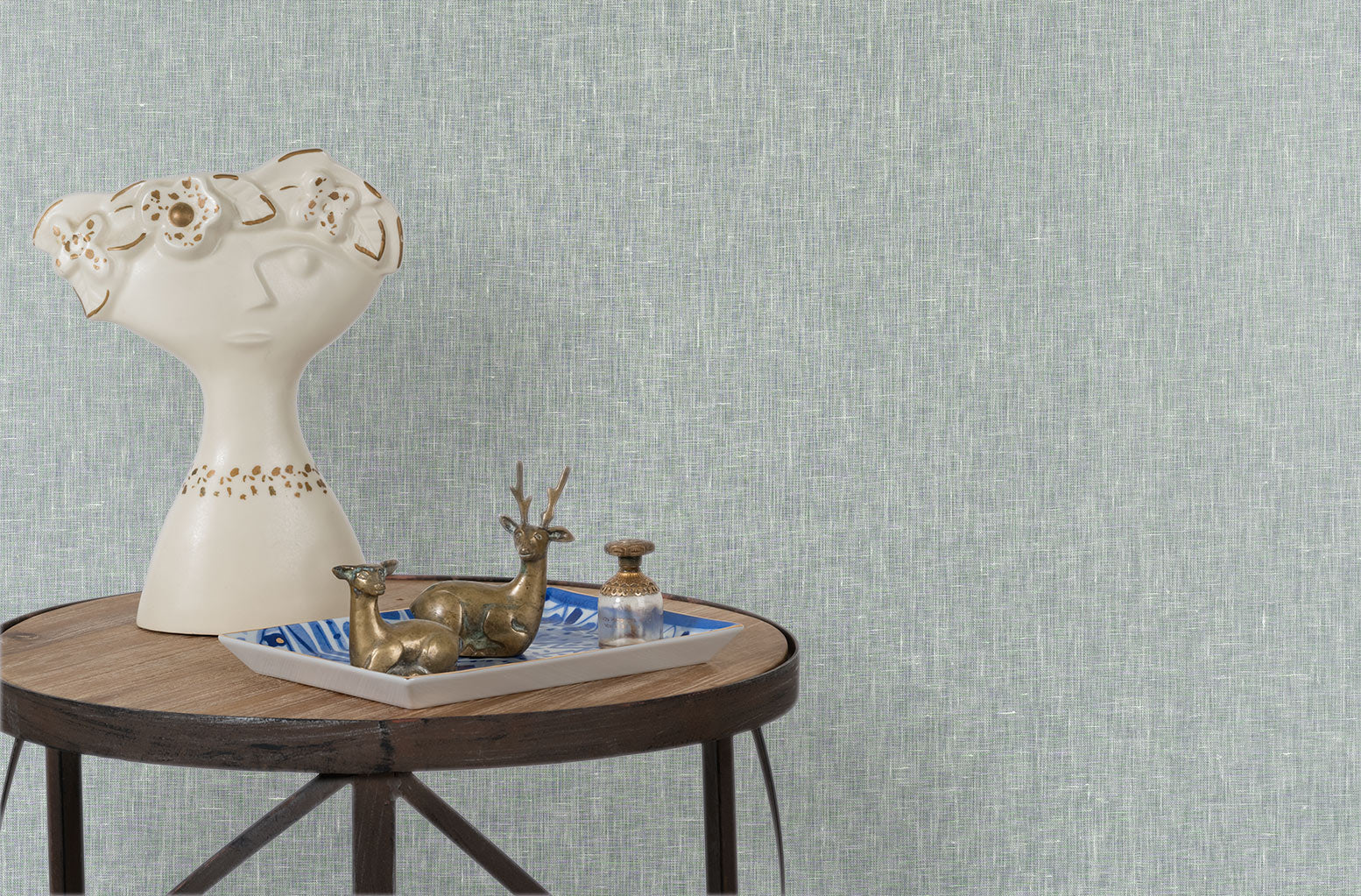 End table with a tray and some sculptures in front of a wall papered in textured grasscloth in pale aqua.