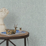 End table with a tray and some sculptures in front of a wall papered in textured grasscloth in pale aqua.