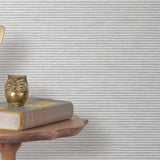 End table with a phone, book and owl sculpture in front of a wall covered in paperweave grasscloth in striped gray.