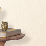 End table with a phone, book and owl sculpture in front of a wall covered in paperweave grasscloth in cream.