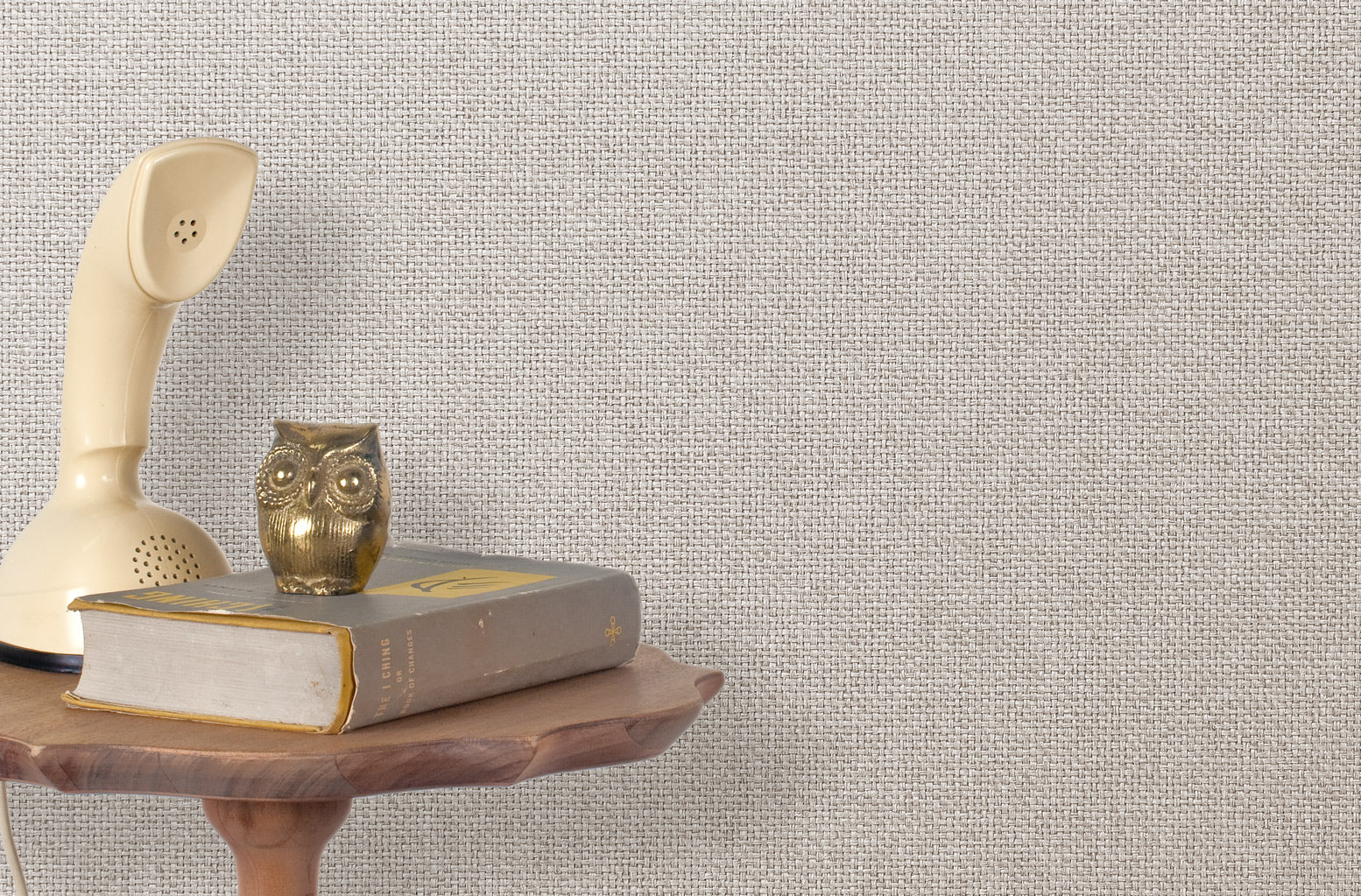 End table with a phone, book and owl sculpture in front of a wall covered in metallic paperweave grasscloth in gray.