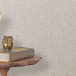 End table with a phone, book and owl sculpture in front of a wall covered in metallic paperweave grasscloth in gray.