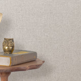 End table with a phone, book and owl sculpture in front of a wall covered in metallic paperweave grasscloth in gray.