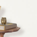 End table with a phone, book and owl sculpture in front of a wall covered in paperweave grasscloth in white.