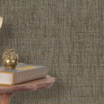 End table with a phone, book and owl sculpture in front of a wall covered in paperweave grasscloth in mottled brown.