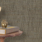 End table with a phone, book and owl sculpture in front of a wall covered in paperweave grasscloth in mottled brown.