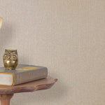 End table with a phone, book and owl sculpture in front of a wall covered in metallic paperweave grasscloth in neutral.