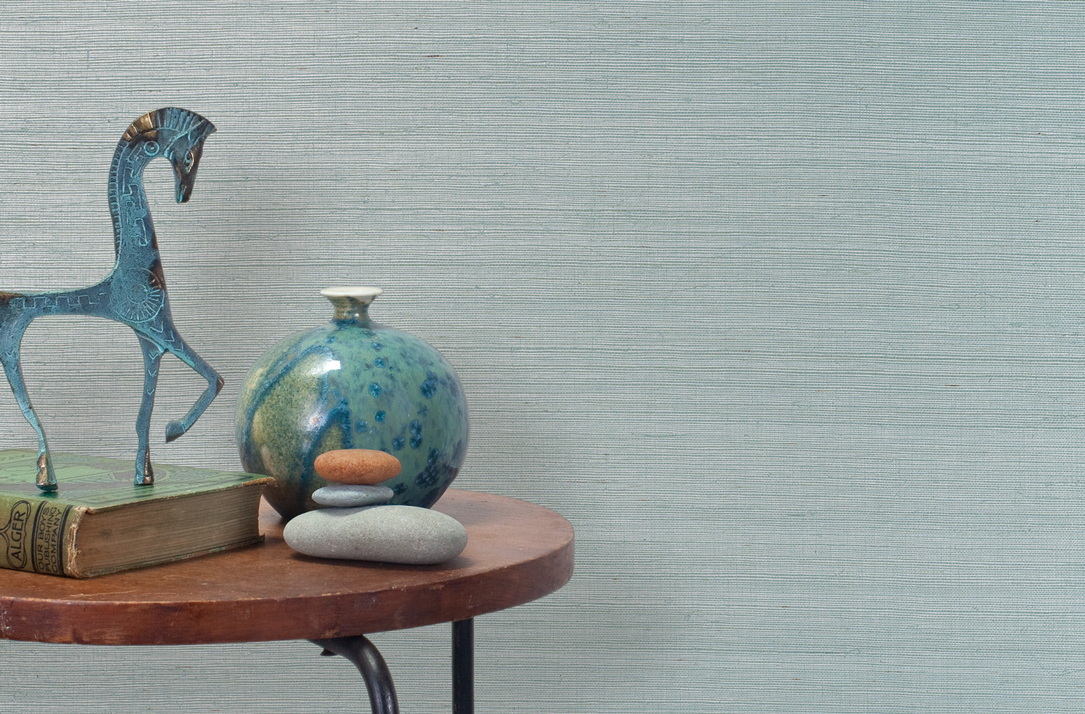 End table with a vase, horse sculpture and stones in front of a wall covered in sisal grasscloth in pastel blue and white.