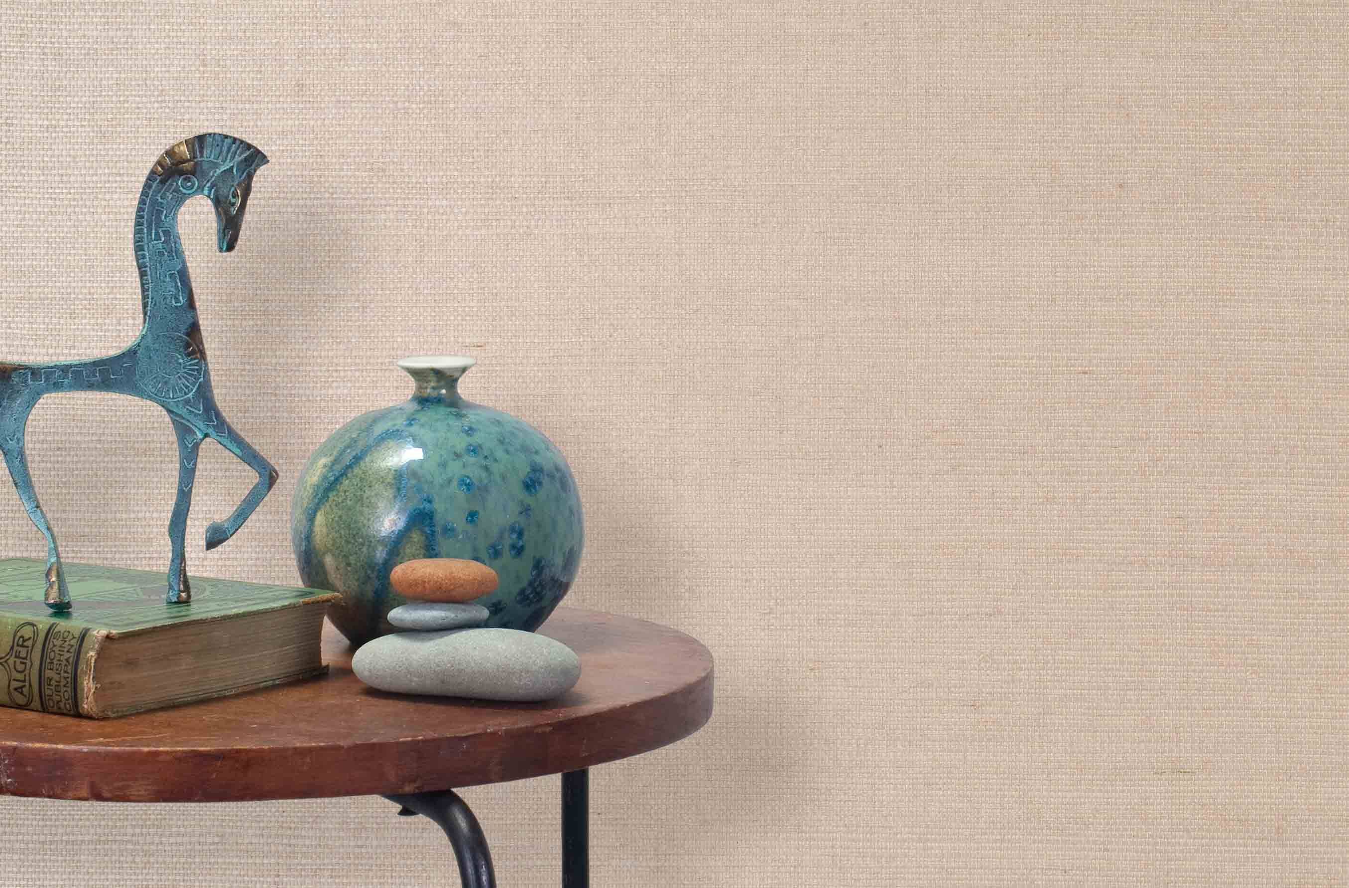 End table with a vase, horse sculpture and stones in front of a wall covered in sisal grasscloth in pale pink.