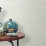 End table with a vase, horse sculpture and stones in front of a wall covered in sisal grasscloth in mottled white and cream.