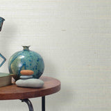 End table with a vase, horse sculpture and stones in front of a wall covered in sisal grasscloth in mottled white and cream.