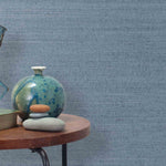 End table with a vase, horse sculpture and stones in front of a wall covered in sisal grasscloth in mottled blue.